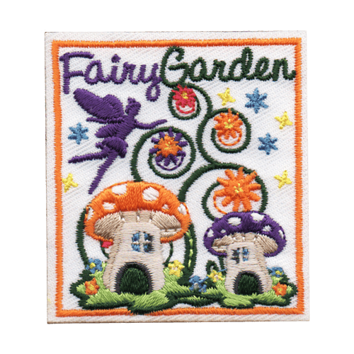 A fairy flies above two mushroom houses placed in a beautiful garden. Vines spiral upwards and bloom into flowers. The words Fairy Garden are stitched at the top.
