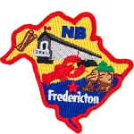 This crest is shaped like the province of New Brunswick. Decorating it are the initials NB, the Heartland Covered Bridge, a lobster, the coast, and the capital city Fredericton.