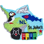 This crest is shaped like the province of Newfoundland and Labrador. Decorating it are the initials NL, a cod with a red kiss mark on it, a dog, a puffin, the ocean, and the capital city St. John's.