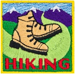 Two hiking boots on a trail that leads into the mountains. The word Hiking is stitched below.