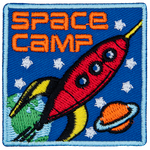 A red rocket blasts through space past Earth and Saturn. The words Space Camp are in the top left corner.