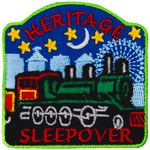 A green train is in the center of the patch, with blue buildings behind it and the night sky. The words Heritage Sleepover are stitched above and below.