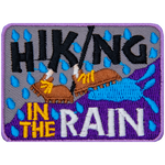 The words Hiking In The Rain surround two brown shoes walking up a hill in the rain.