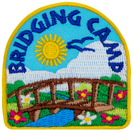A wooden bridge connects two sides of a grassy field dotted with flowers. A blue stream runs peacefully under the bridge as birds soar in the sunny sky overhead.