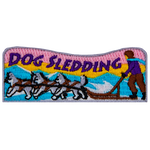 The words Dog Sledding are above a dog sled pulled by three dogs.
