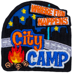 The words Where Fun Happens are on a signpost. Below them, overtop a road are the words City Camp and a campfire. The back is a night skyline.