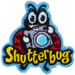A ladybug holds up a retro camera. The word Shutterbug is stitched across the bottom.  Photography.