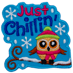 A little owl is bundled up in a toque and scarf as it sits on a snow-covered tree branch. The text Just Chillin' sits above it.