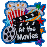 A clapperboard with the words At The Movie rests against a popcorn bucket. A roll of film is next to it.