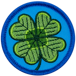 This circular patch displays a four-leaf shamrock on a background of blue.
