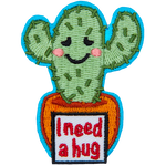 A two-armed cactus has an embarrassed smile as the sign in front of its pot reads I need a hug.