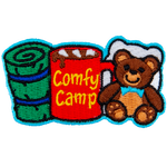From left to right is a sleeping bag, a mug of coco with the words 'Comfy Camping' on the side, and a teddy bear with a pillow behind it.