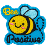 A cute bee has dots for eyes and a big U-shaped smile. The words Bee Positive are stitched above and below the bee. 