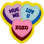Three candy hearts have text on them. One says Hug Me, one says Luv U, and the last has XOXO.