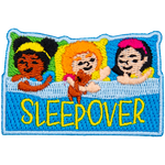 Three little girls are pretending to be asleep in bed. The word Sleepover is across the blanket.