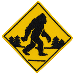A yellow road sign with a Sasquatch crossing the road.