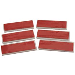 A pile of pin-backs rests in the center of this photo. Below the pile are two pin backs, one showing the adhesive side and the other displaying an open pin.