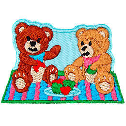 Two teddy bears sit on a picnic blanket eating red and green apples on a clear day.