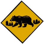A monochromatic bear walks across a yellow caution sign.