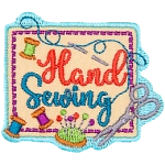 A square piece of fabric with three spools of thread, scissors, a sewing needle and the words Hand Sewing on top of it.