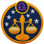 This circular crest displays the scales of justice surrounded by stars. The sign of Libra sits above it.