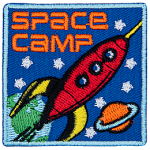 A red rocket blasts through space past Earth and Saturn. The words Space Camp are in the top left corner.