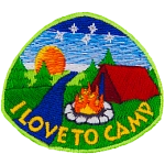A red tent sits behind a campfire. The sun is setting in the background, and a stream runs past the camp.