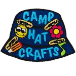 A blue camp hat has little crafts pinned to it. The text Camp Hat Crafts is embroidered on the side.