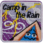 A tent with a scared expression on it watches a lightning storm. The words Camp In The Rain are above it.