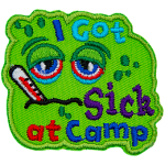 A green patch with a sad face. The words I Got Sick At Camp are on it.