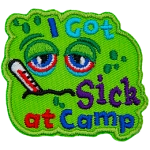 A green patch with a sad face. The words I Got Sick At Camp are on it.