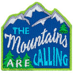 The words The Mountains Are Calling are stitched across a mountain range with pine trees. 