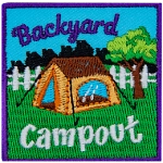 A brown tent is in a backyard in front of a white fence. The words Backyard Campout are above and below it.