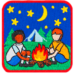 Two kids sit around a campfire with the night sky and a tent behind them. 