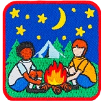 Two kids sit around a campfire with the night sky and a tent behind them. 