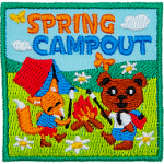 An anthropomorphic bear and a fox roast marshmallows over a campfire. A tent is behind them in an open meadow. Spring Campout is stitched above.