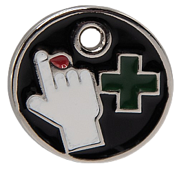 This circular metal charm depicts a green cross next to a hand with a blood drop coming out of a finger.