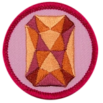 An orange sapphire is in the centre of a circular pink badge.