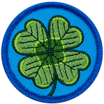 This circular patch displays a four-leaf shamrock on a background of blue.