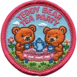 Two teddy bears sit in the grass at a table with a blue tea set.