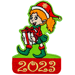 A happy elf with a wide smile and a ponytail of red hair carries a white present with a red ribbon. The date 2023 is below them.