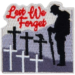 A soldier stands with his head bowed in front of several crosses. The words Lest We Forget are in the sky.
