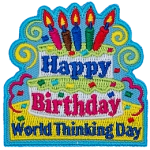 A two-tiered birthday cake with candles and the words Happy Birthday on it. Below the cake are the words World Thinking Day.
