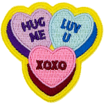 Three candy hearts have text on them. One says Hug Me, one says Luv U, and the last has XOXO.