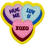 Three candy hearts have text on them. One says Hug Me, one says Luv U, and the last has XOXO.