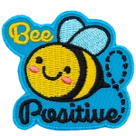 A cute bee has dots for eyes and a big U-shaped smile. The words Bee Positive are stitched above and below the bee. 