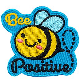 A cute bee has dots for eyes and a big U-shaped smile. The words Bee Positive are stitched above and below the bee.