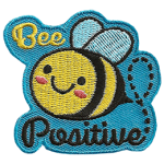 A cute bee has dots for eyes and a big U-shaped smile. The words Bee Positive are stitched above and below the bee. 