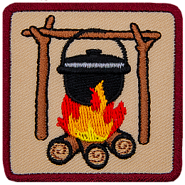 A black iron pot hangs from a high bar suspended on forks which are all made from branches. The pot simmers over a roaring campfire.