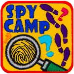 A magnifying glass magnifies a fingerprint. The words Spy Camp are above it, and the right side has shoe prints.